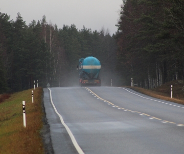 A truck tank vehicle driving down a misty road along many green trees