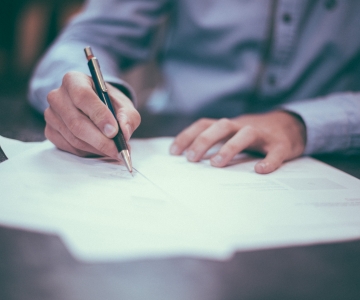 A person signing a piece of paper with a pen.